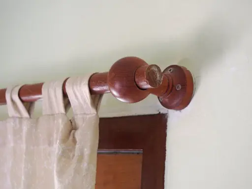 Drewniany karnisz z ozdobną kulą, zasłona w neutralnym kolorze. Karnisz inspiracje dla miłośników naturalnych materiałów.
