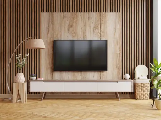 Nowoczesny salon z telewizorem na tle pionowych lamelek. Drewniana okładzina i meble tworzą przytulną atmosferę.