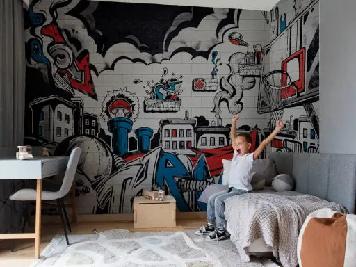 Chłopiec cieszy się w pokoju z dynamicznym **graffiti w pokoju** na ścianie, przedstawiającym miasto i elementy koszykówki.