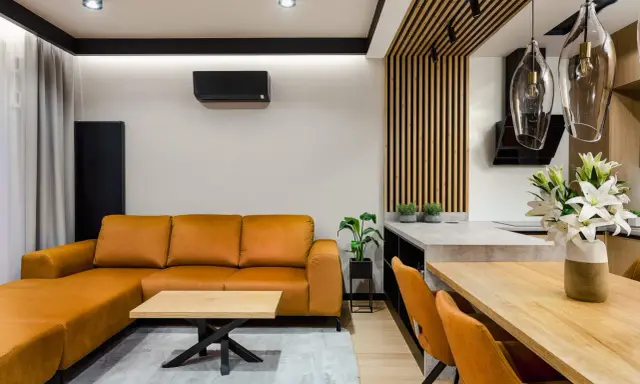 Nowoczesny salon bez sufitu z pomarańczową kanapą, drewnianym stołem i designerskimi lampami.