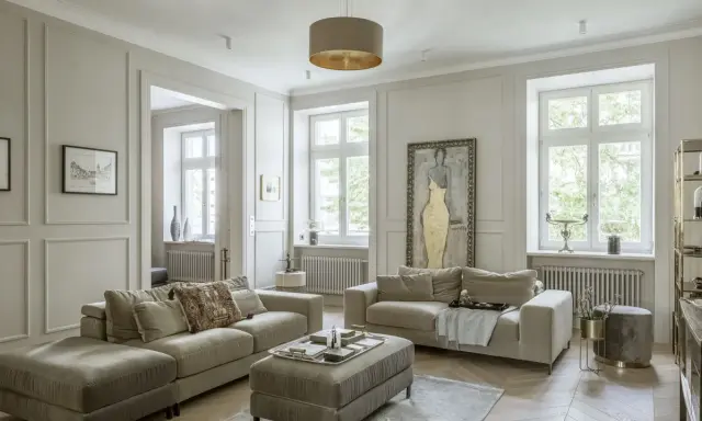 Elegancki salon z dwoma beżowymi sofami, ozdobną sztukaterią na ścianach i dużym obrazem.