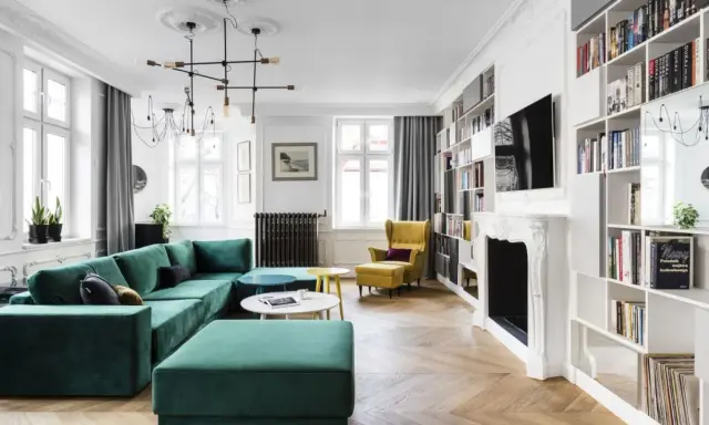 Elegancki salon w stylu paryskim z zieloną kanapą, żółtym fotelem i regałami pełnymi książek.