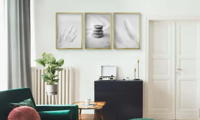 Trzy minimalistyczne plakaty w złotych ramach nad ciemną komodą. Dowiedz się, jak powiesić plakat bez niszczenia ścian.