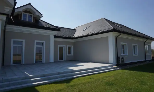 Nowoczesny dom z tarasem i trawnikiem. Elegancki gzyms co to? To ozdobny element architektoniczny podkreślający linię dachu.