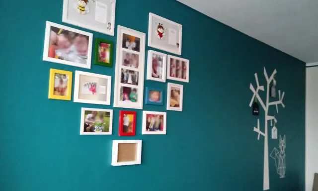 Galeria zdjęć na turkusowej ścianie, z motywem drzewa i lisa po prawej stronie.