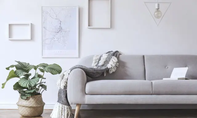 Przytulny salon z szarą kanapą, ozdobioną narzutą. Na ścianie mapa Sydney i geometryczna lampa.