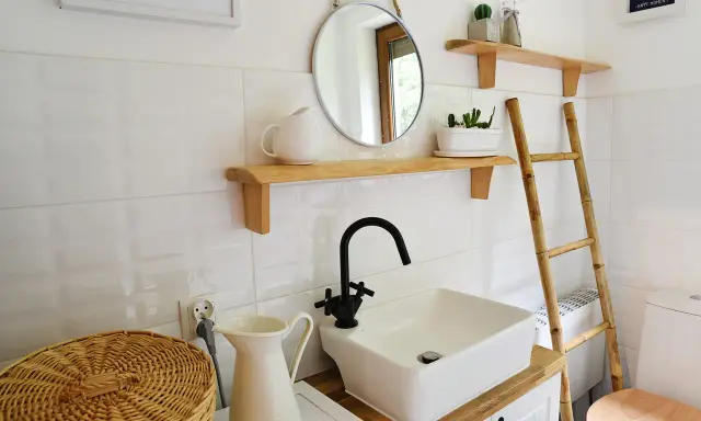 Urocza, mała łazienka w stylu retro z białymi kafelkami, drewnianymi półkami, okrągłym lustrem i bambusową drabiną.