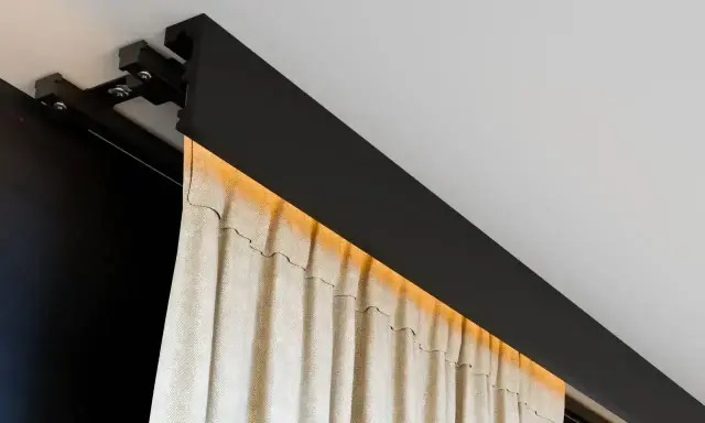 Nowoczesna szyna sufitowa z ukrytym oświetleniem LED, na której wiszą beżowe zasłony. Eleganckie rozwiązanie zamiast tradycyjnego karnisza.