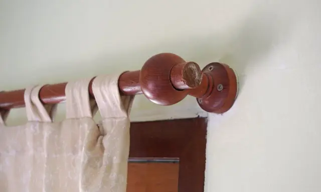 Drewniany karnisz z ozdobną kulą, zasłona w neutralnym kolorze. Karnisz inspiracje dla miłośników naturalnych materiałów.