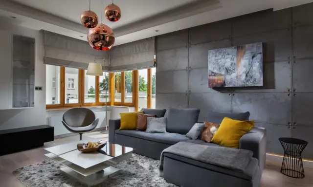 Nowoczesny salon z betonową ścianą. Inspiracje dla odważnych: szara sofa, miedziane lampy i geometryczne meble tworzą industrialny klimat.