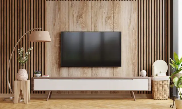 Nowoczesny salon z telewizorem na tle pionowych lamelek. Drewniana okładzina i meble tworzą przytulną atmosferę.