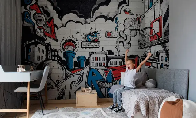 Chłopiec cieszy się w pokoju z dynamicznym **graffiti w pokoju** na ścianie, przedstawiającym miasto i elementy koszykówki.