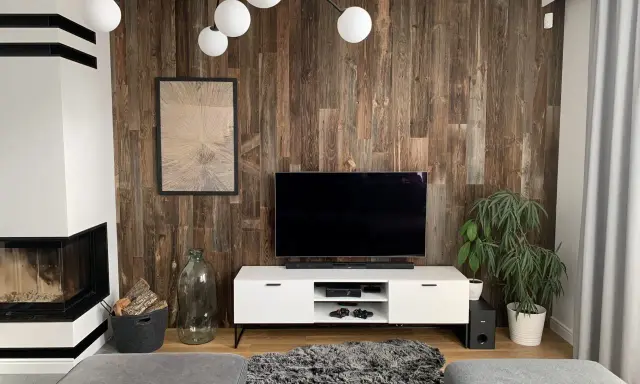 Nowoczesny salon z kominkiem i telewizorem na tle ściany z desek. Tapeta stare deski nadaje wnętrzu rustykalny charakter.
