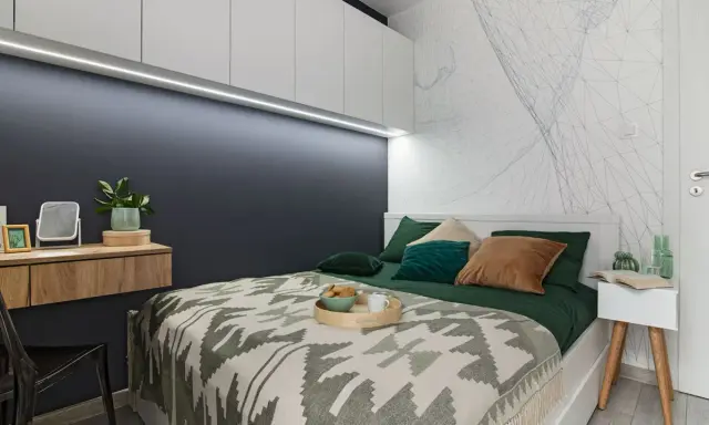 Nowoczesny wystrój sypialni z geometryczną tapetą, drewnianą toaletką i wygodnym łóżkiem.