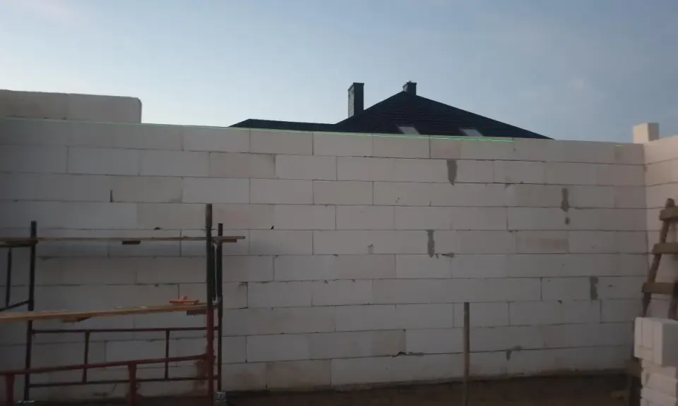 Budowa domu z bloczków, zielona linia laserowa wyznacza poziom. To dobry pomysł na krzywe ściany, jeśli chcesz uzyskać ciekawy efekt architektoniczny.