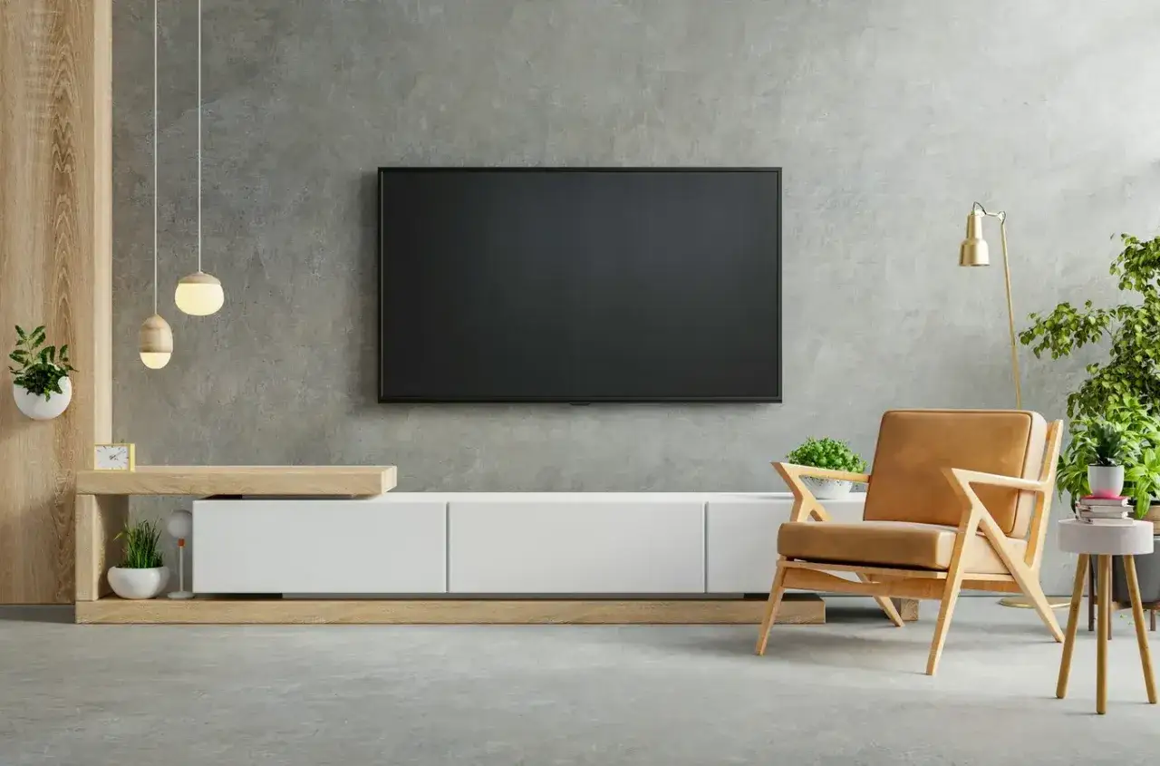 Nowoczesny salon z telewizorem na betonowej ścianie, wygodnym fotelem i roślinami.