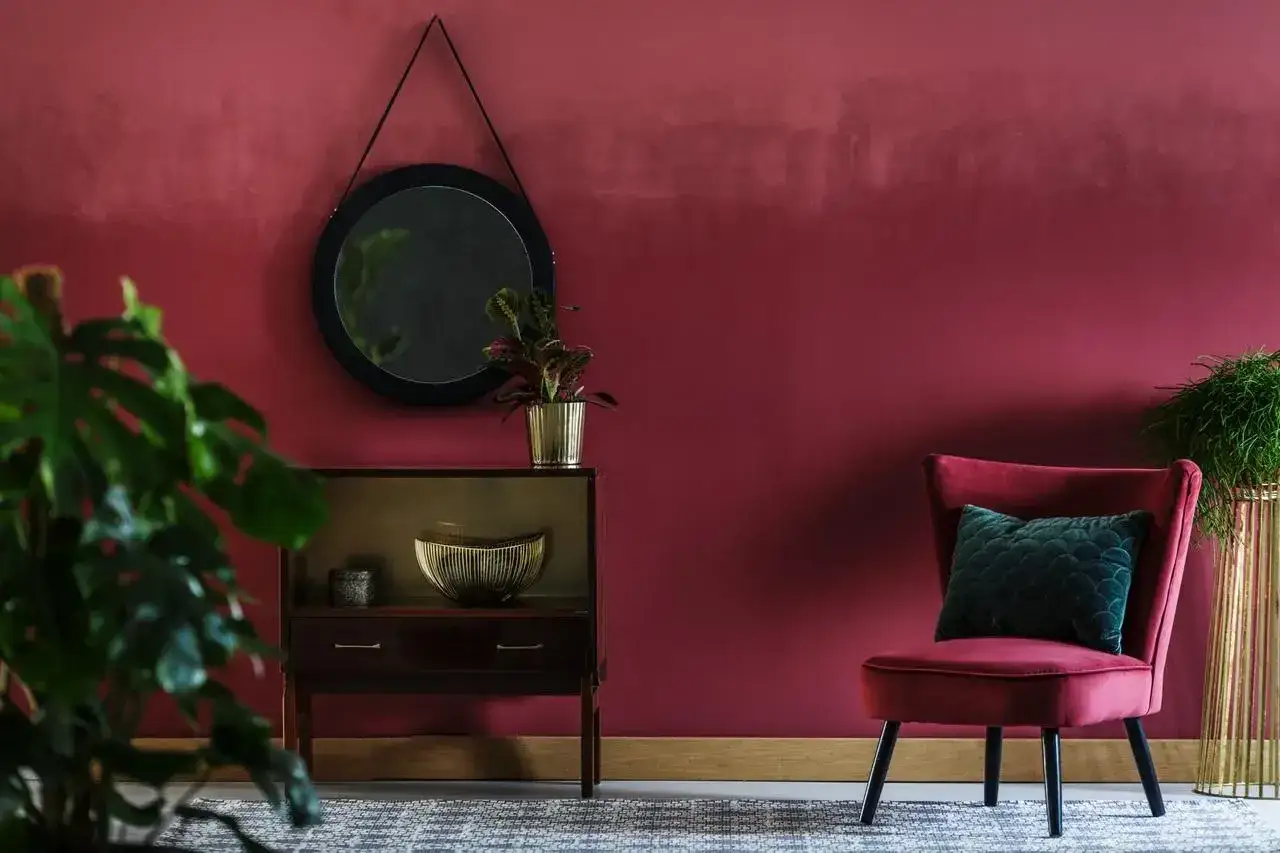 Elegancki salon z burgundowymi ścianami, aksamitnym fotelem i stylową komodą.