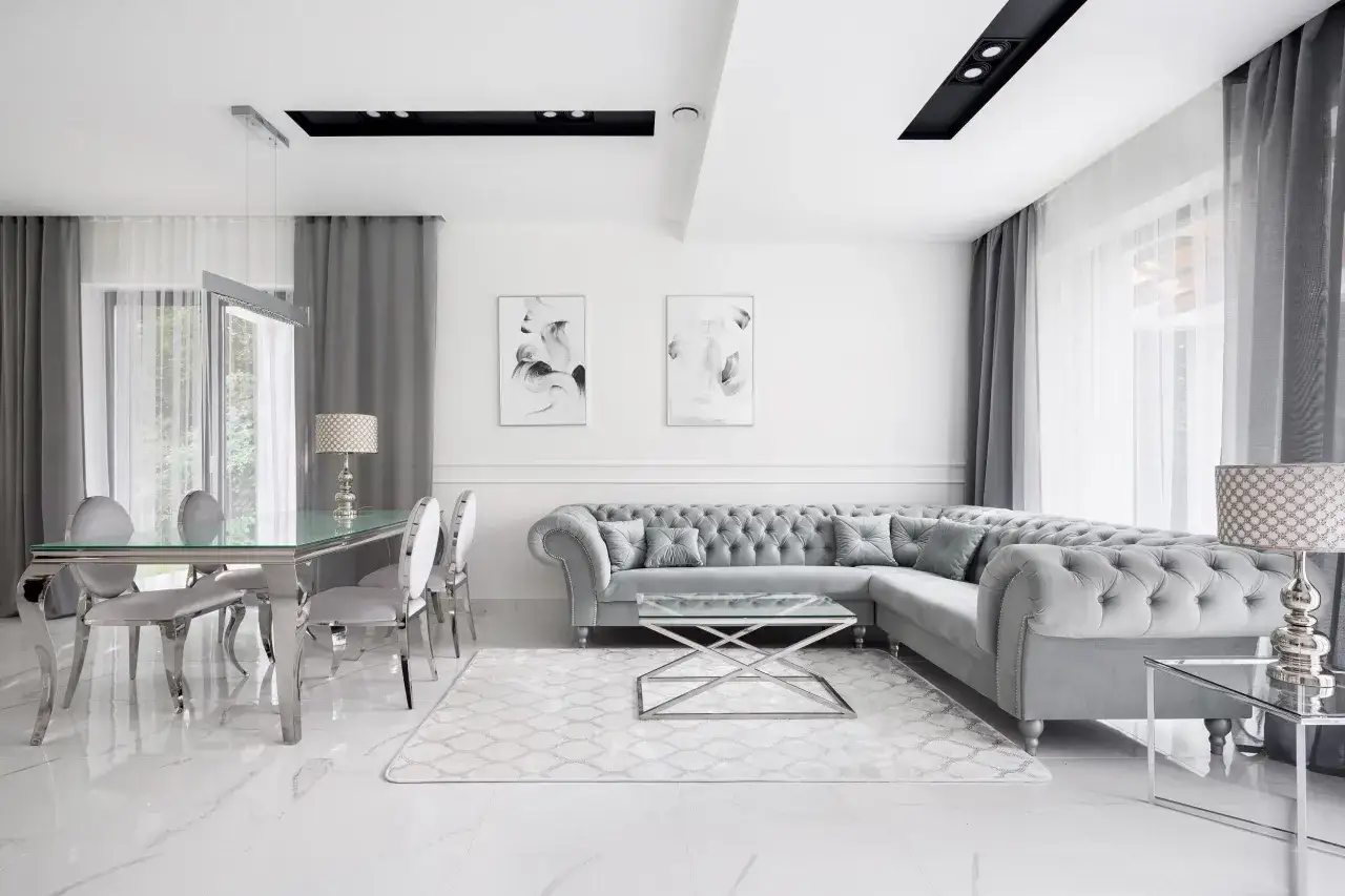 Eleganckie wnętrze w stylu nowojorskim: szara sofa chesterfield, szklany stół z krzesłami, dywan i nowoczesne oświetlenie.