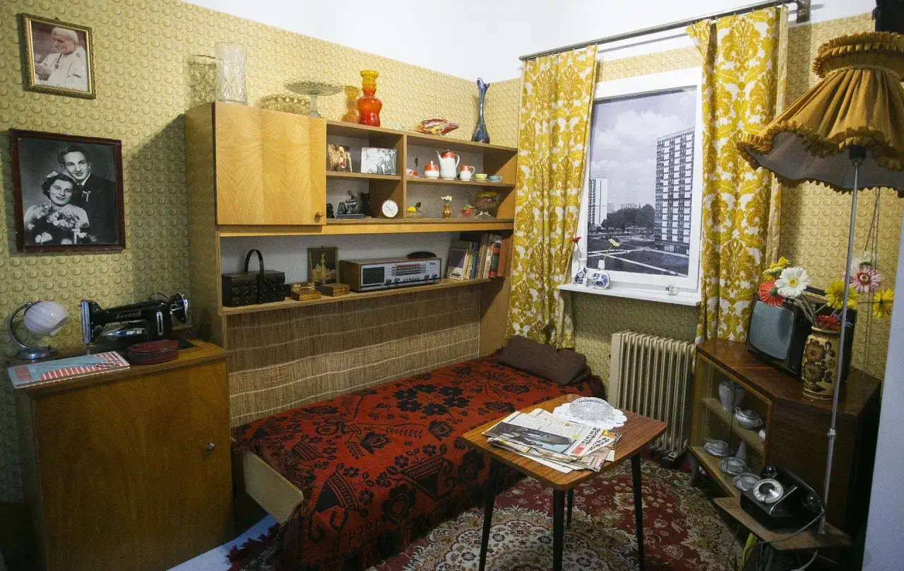 Pok&oacute;j lata 80. z ł&oacute;żkiem, maszyną do szycia, radiem i telewizorem.