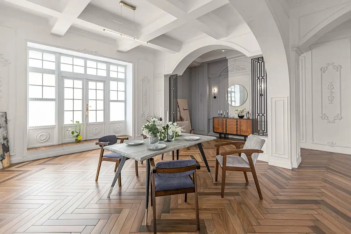 Elegancki salon z łukiem, inspiracja czym wykończyć łuk w salonie. Drewniana podłoga w jodełkę, stół z krzesłami, komoda i okrągłe lustro.