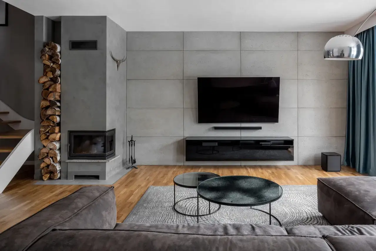 Nowoczesny salon z betonową ścianą, kominkiem, telewizorem i wygodną sofą.