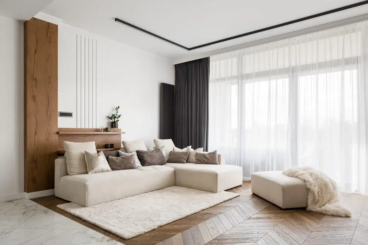 Nowoczesny salon z beżową kanapą i puszystym dywanem. Zasłony wiszą na ukrytym karniszu w suficie, tworząc elegancką linię.