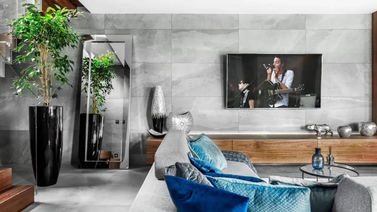 Nowoczesna ściana TV glamour z szarego kamienia, z dużym lustrem, roślinami w donicach i wygodną kanapą.