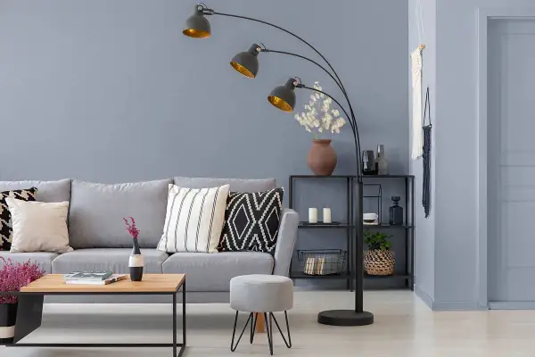 Przytulny salon z szarą kanapą, stolikiem kawowym i łukową lampą. Ciepły szary kolor ścian tworzy relaksującą atmosferę.