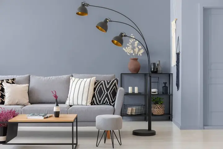 Przytulny salon z szarą kanapą, stolikiem kawowym i łukową lampą. Ciepły szary kolor ścian tworzy relaksującą atmosferę.