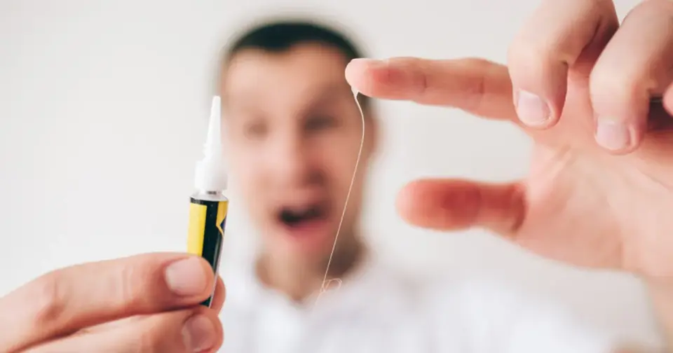 Zastanawiasz się, czym zmyć super glue z rąk? Na zdjęciu widać tubkę kleju i palce z przyklejoną nitką.